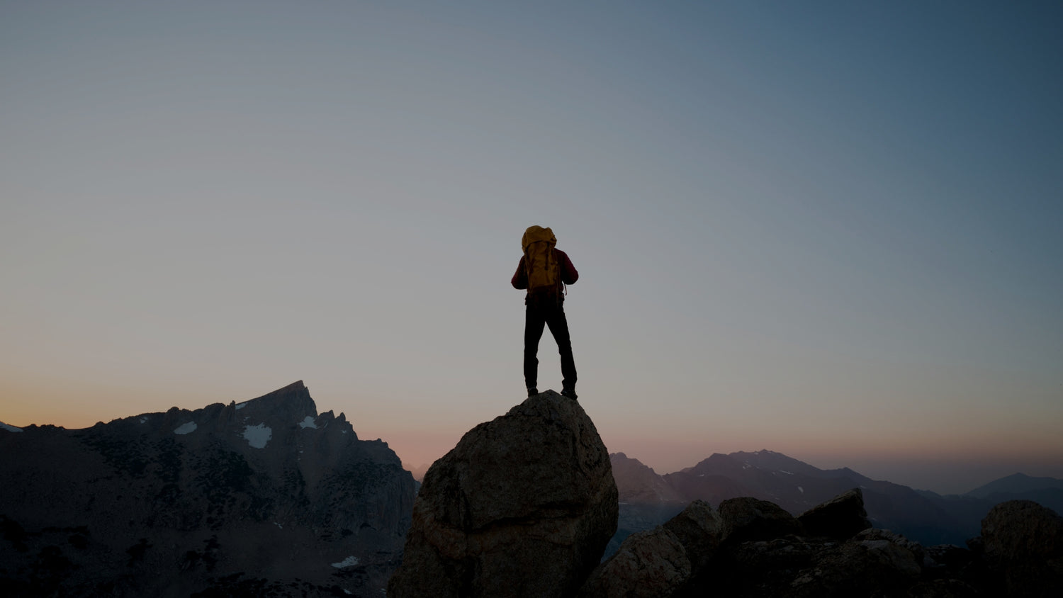Person standing on a mountain peak at sunset with a backpack