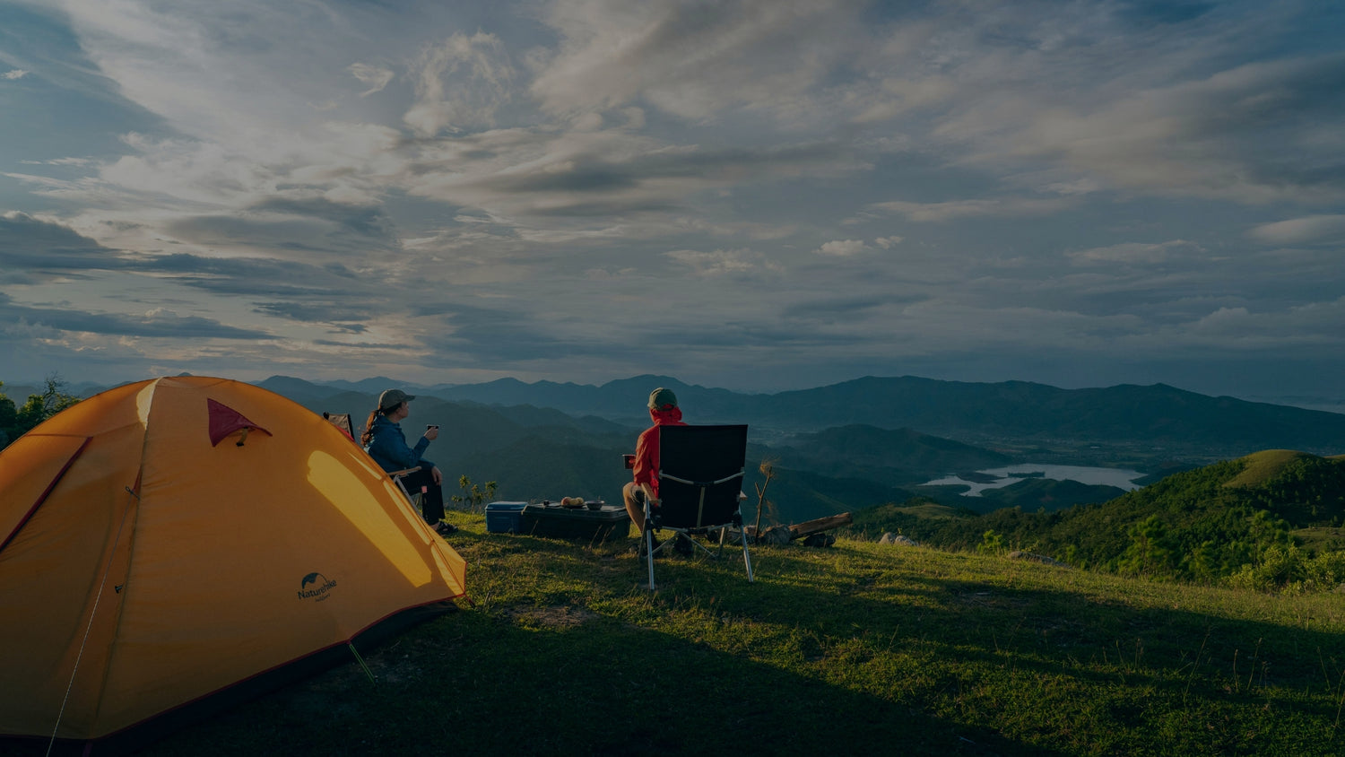 Two people camping on a mountain with a yellow tent and scenic view.
