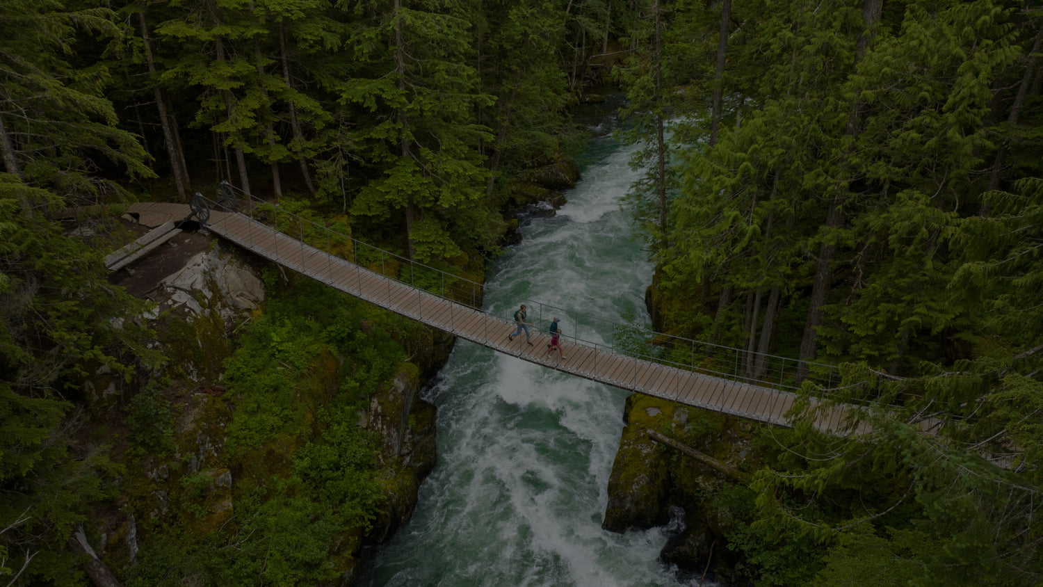 Hikers crossing suspension bridge over rushing turquoise river in forest